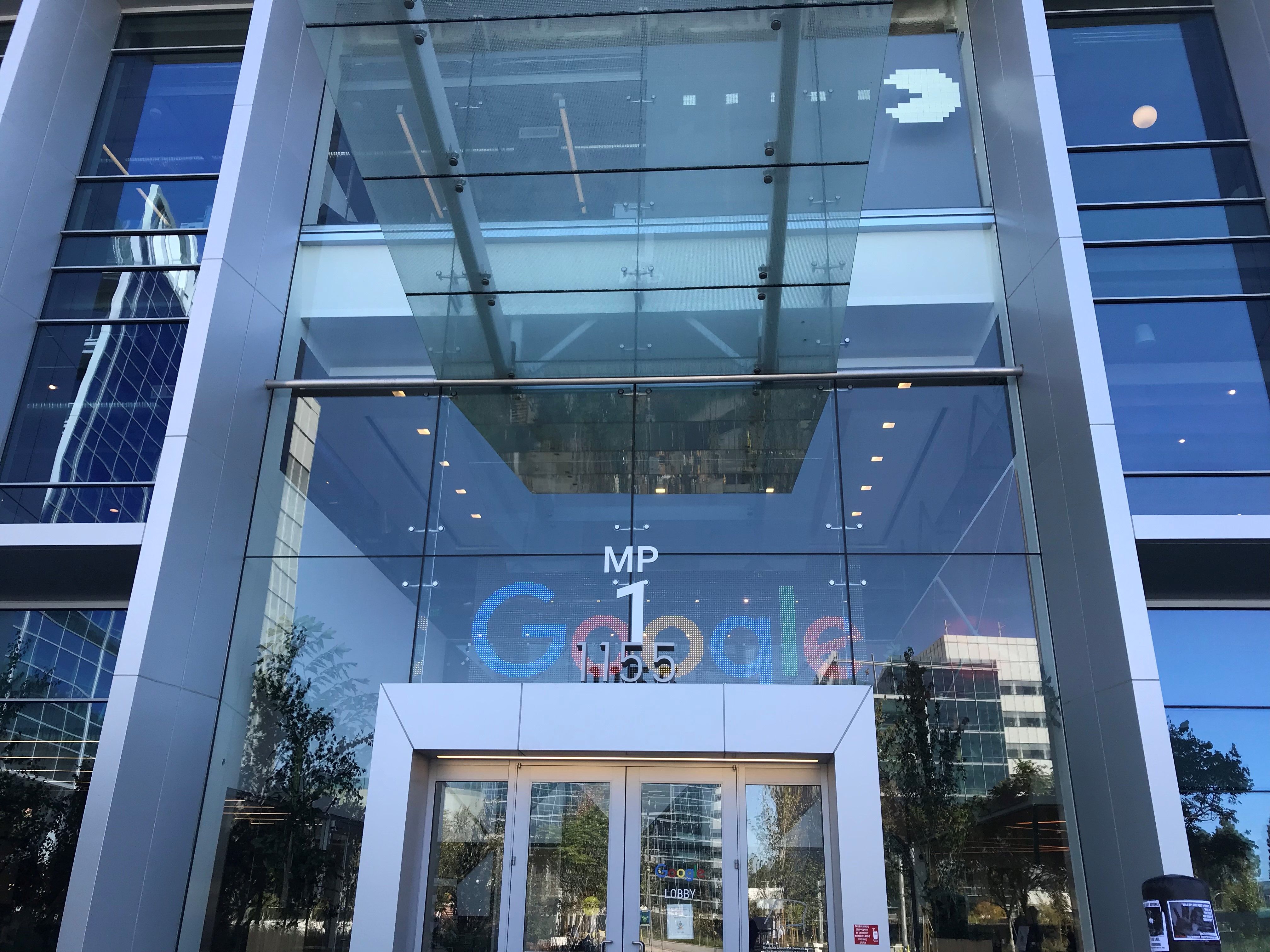 The exterior of a Google building with glass front windows and an 8-bit Packman in the top right of the building's front window